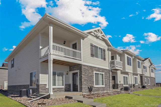 rear view of house with cooling unit, a balcony, and a yard