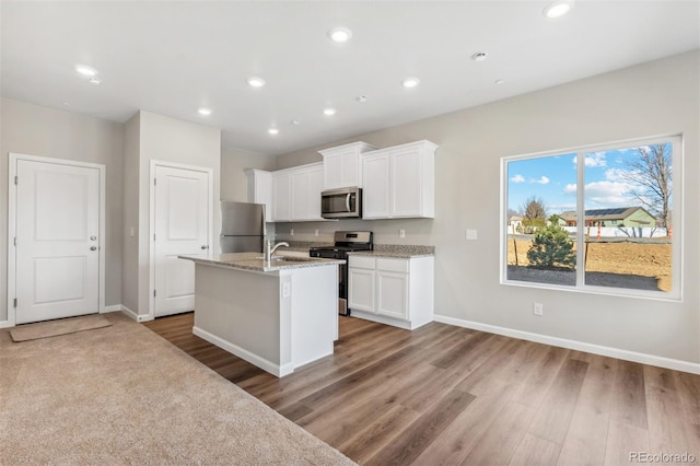 kitchen with a kitchen island with sink, hardwood / wood-style floors, white cabinets, and stainless steel appliances