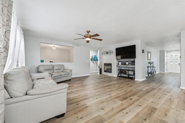 living room with a fireplace, a textured ceiling, light wood-type flooring, and ceiling fan