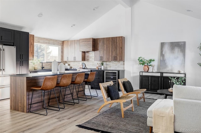 kitchen featuring beverage cooler, light wood-style flooring, freestanding refrigerator, decorative backsplash, and a kitchen bar