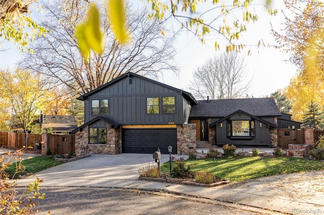 tri-level home featuring board and batten siding, fence, driveway, stone siding, and an attached garage