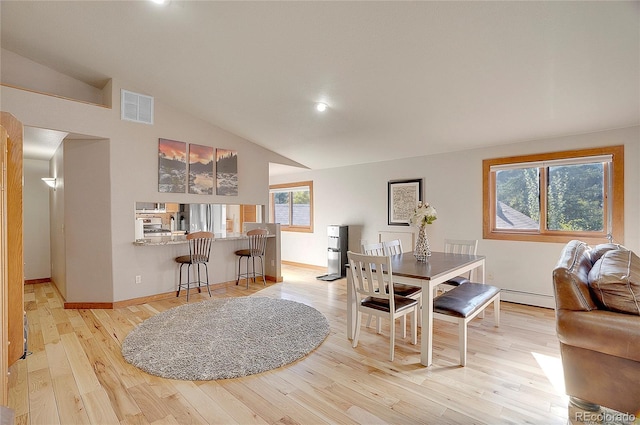 dining area with light hardwood / wood-style floors, vaulted ceiling, and a baseboard heating unit