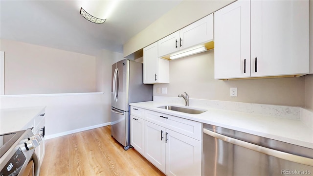 kitchen featuring light wood finished floors, stainless steel appliances, light countertops, white cabinets, and a sink