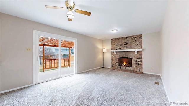 unfurnished living room with carpet floors, visible vents, a ceiling fan, a brick fireplace, and baseboards