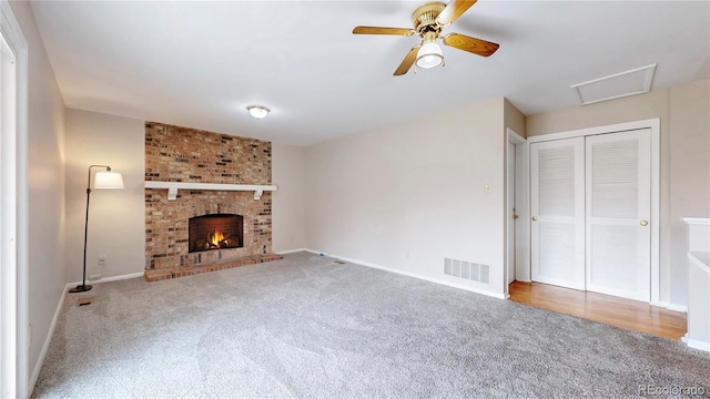 unfurnished living room featuring attic access, baseboards, visible vents, carpet flooring, and a fireplace