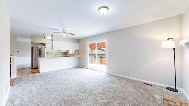 unfurnished living room featuring light colored carpet, visible vents, a sink, ceiling fan, and baseboards