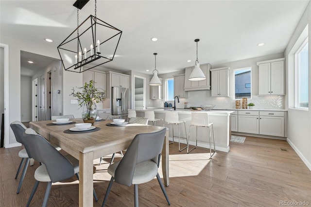 dining room with light wood-type flooring, sink, and a chandelier