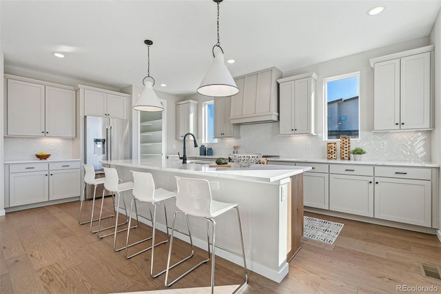 kitchen featuring light wood-type flooring, an island with sink, premium range hood, and sink