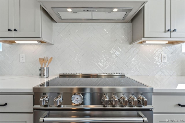 kitchen featuring light stone countertops, backsplash, stove, gray cabinets, and exhaust hood