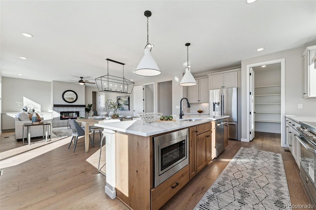 kitchen featuring appliances with stainless steel finishes, a kitchen island with sink, sink, decorative light fixtures, and white cabinetry