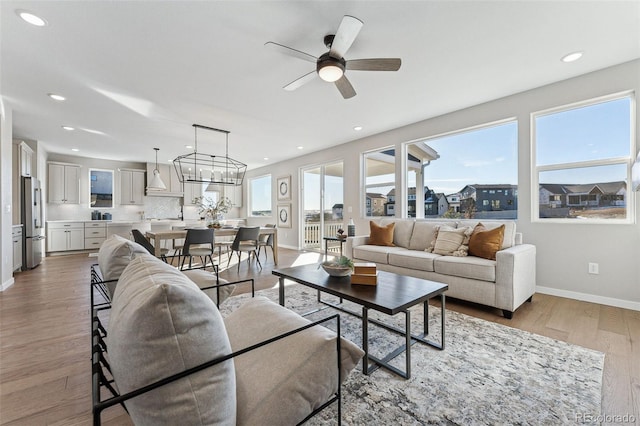 living room featuring ceiling fan with notable chandelier and light hardwood / wood-style flooring