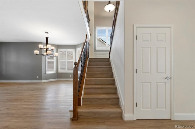 staircase with a notable chandelier, baseboards, and wood finished floors