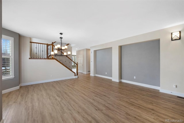 unfurnished living room with a notable chandelier, stairway, baseboards, and wood finished floors