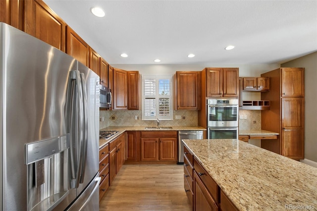 kitchen with tasteful backsplash, brown cabinetry, light wood-style flooring, light stone counters, and stainless steel appliances