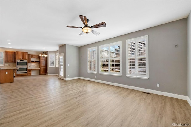 unfurnished living room with light wood-style floors, plenty of natural light, baseboards, and ceiling fan with notable chandelier