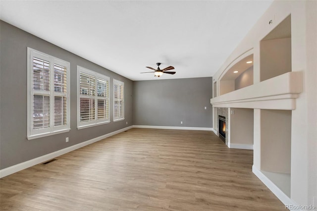 unfurnished living room featuring a ceiling fan, a glass covered fireplace, light wood finished floors, and baseboards