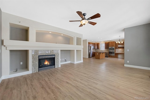 unfurnished living room featuring baseboards, a tiled fireplace, ceiling fan with notable chandelier, light wood-type flooring, and recessed lighting