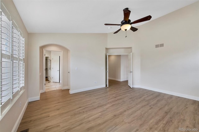 spare room featuring arched walkways, light wood finished floors, lofted ceiling, visible vents, and baseboards