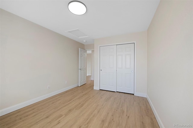 unfurnished bedroom featuring light wood-style floors, attic access, baseboards, and a closet