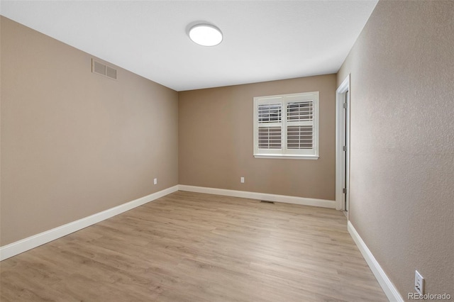 spare room featuring light wood-style flooring, visible vents, and baseboards