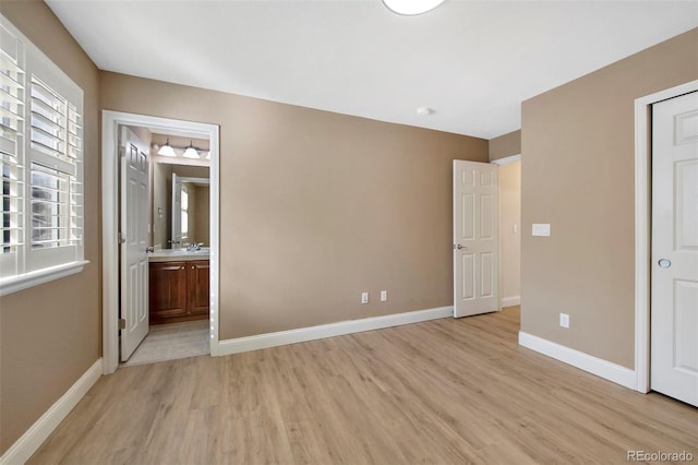 unfurnished bedroom featuring multiple windows, ensuite bath, light wood-style flooring, and baseboards