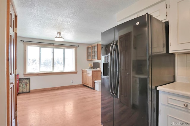 10771 Winding Meadow Dr, Kiowa, CO 80117 - kitchen featuring light wood finished floors, baseboards, glass insert cabinets, light countertops, and black fridge