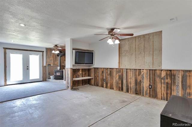 10771 Winding Meadow Dr, Kiowa, CO 80117 - unfurnished living room featuring a wainscoted wall, a wood stove, a textured ceiling, wood walls, and concrete floors