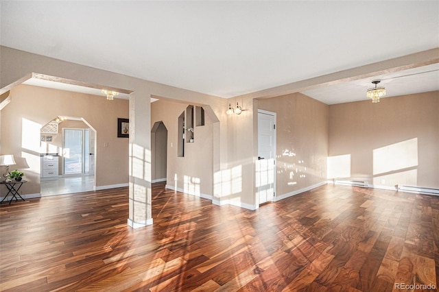 spare room featuring arched walkways, baseboard heating, wood finished floors, and baseboards