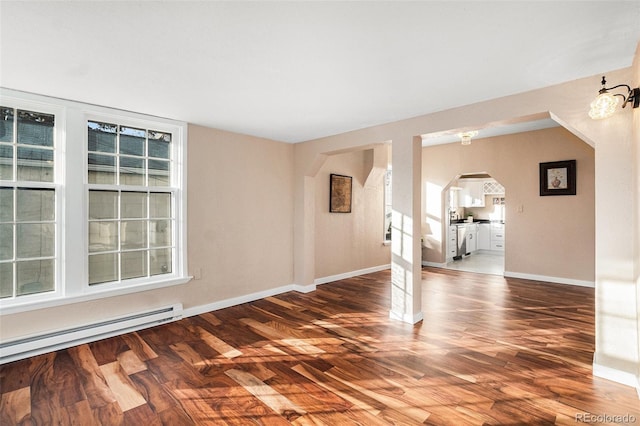 spare room featuring arched walkways, a baseboard heating unit, wood finished floors, and baseboards