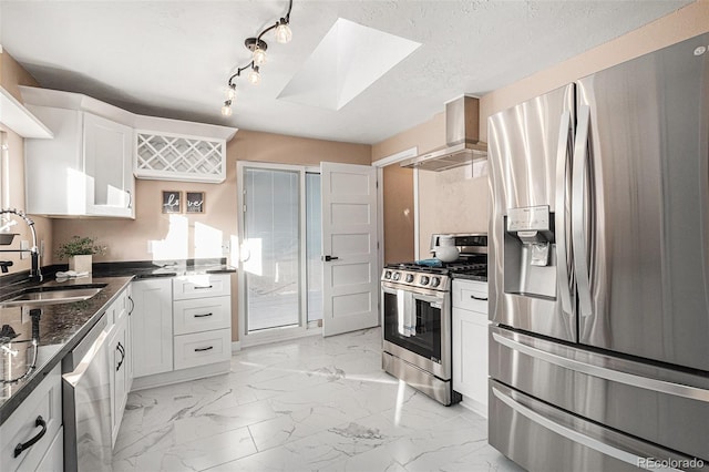 kitchen featuring stainless steel appliances, a skylight, a sink, marble finish floor, and wall chimney exhaust hood