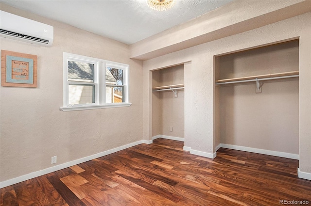 unfurnished bedroom with baseboards, a textured wall, dark wood-style flooring, a wall mounted air conditioner, and multiple closets