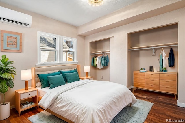 bedroom with dark wood-style floors, baseboards, two closets, and a wall mounted air conditioner