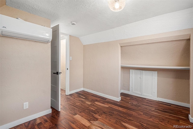 unfurnished bedroom featuring a textured ceiling, lofted ceiling, wood finished floors, baseboards, and a wall mounted air conditioner