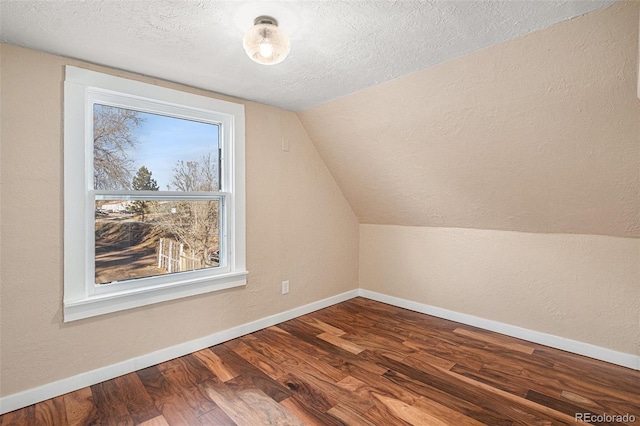 additional living space featuring a textured ceiling, a textured wall, wood finished floors, baseboards, and vaulted ceiling