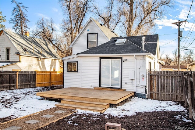 snow covered property with a fenced backyard, roof with shingles, and a wooden deck