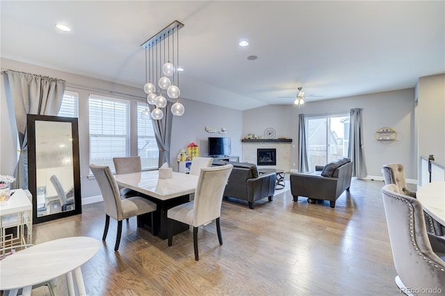 dining area featuring baseboards, a glass covered fireplace, ceiling fan, wood finished floors, and recessed lighting