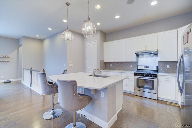 kitchen featuring light wood finished floors, decorative backsplash, appliances with stainless steel finishes, extractor fan, and a sink