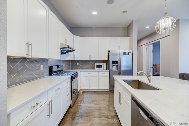 kitchen with stainless steel appliances, light stone counters, a sink, and under cabinet range hood