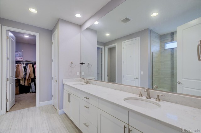 full bath with a tile shower, double vanity, a sink, and visible vents