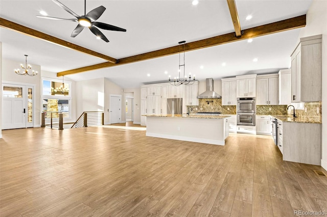 kitchen with a spacious island, pendant lighting, appliances with stainless steel finishes, wall chimney range hood, and vaulted ceiling with beams