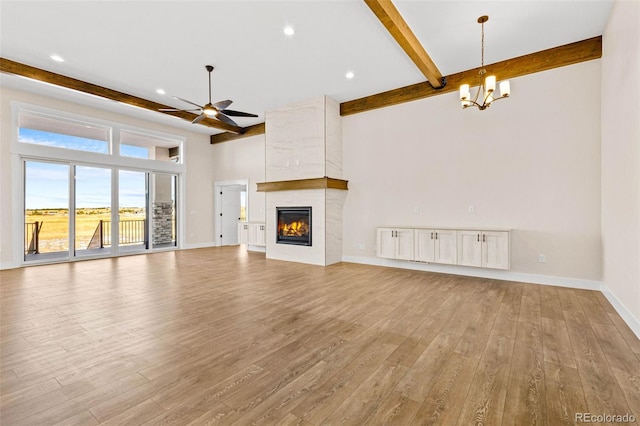 unfurnished living room with ceiling fan with notable chandelier, light hardwood / wood-style flooring, beam ceiling, and a fireplace