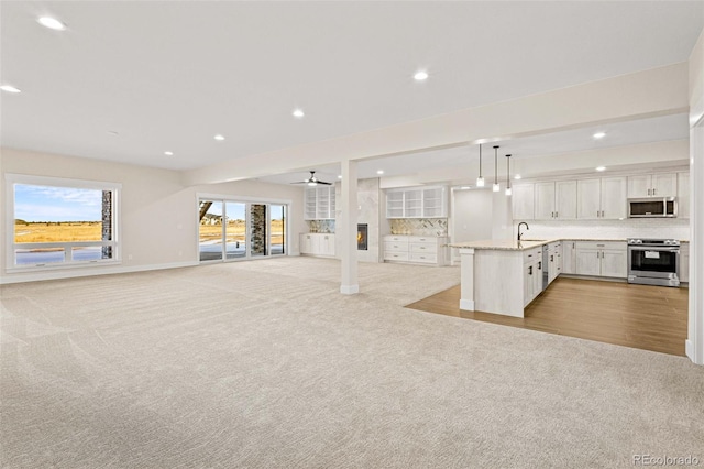 unfurnished living room featuring sink, ceiling fan, and light colored carpet