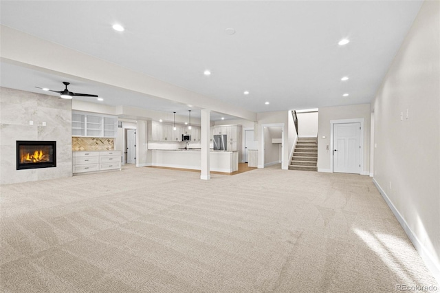 unfurnished living room featuring ceiling fan, a tile fireplace, and light carpet