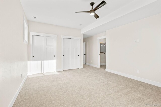 unfurnished bedroom featuring ceiling fan, connected bathroom, light carpet, and multiple closets