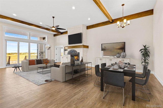 living room featuring light wood-type flooring, ceiling fan with notable chandelier, a high end fireplace, and beam ceiling