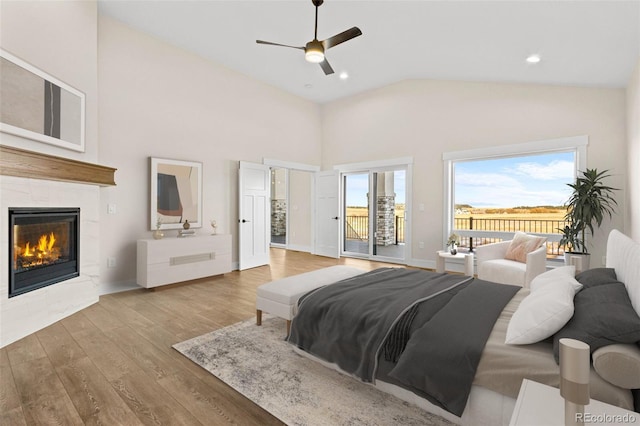 bedroom with ceiling fan, a tiled fireplace, access to exterior, high vaulted ceiling, and light hardwood / wood-style floors