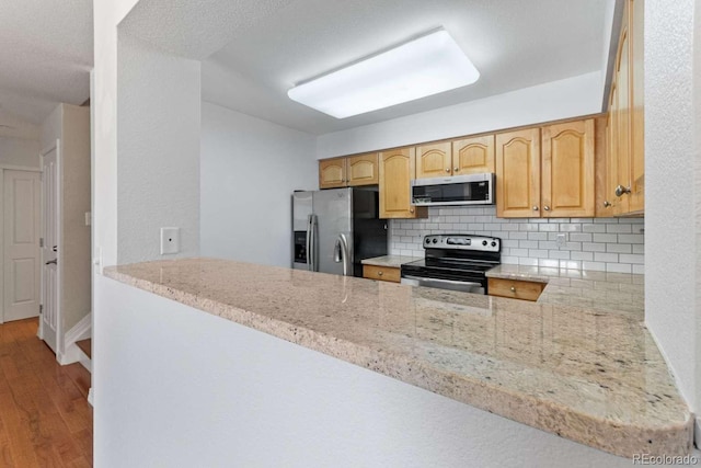 13231 Holly St Unit B, Thornton, CO 80241 - kitchen with appliances with stainless steel finishes, backsplash, light stone countertops, wood finished floors, and a peninsula