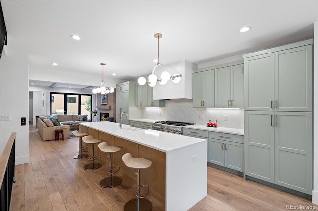 kitchen featuring a breakfast bar area, range, decorative light fixtures, an island with sink, and backsplash