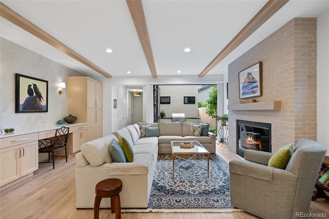 living room with beamed ceiling, built in desk, a brick fireplace, and light wood-type flooring