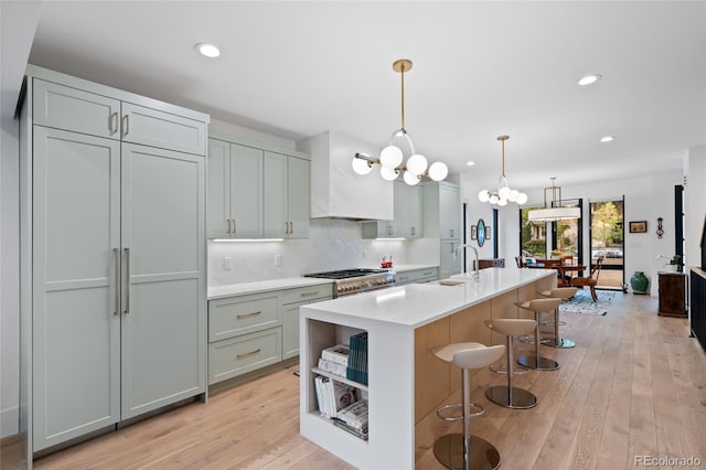 kitchen with premium range hood, a breakfast bar, hanging light fixtures, a center island with sink, and backsplash